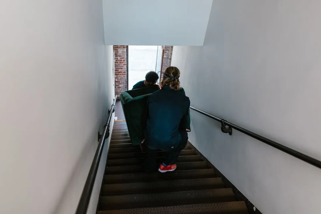 Zwei Personen tragen ein Sofa über den Gehweg